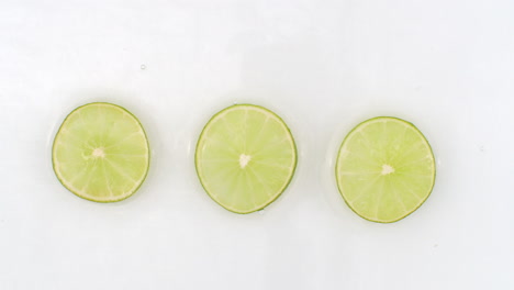 Drops-of-water-fall-on-three-pieces-of-lime-lying-on-a-white-background.
